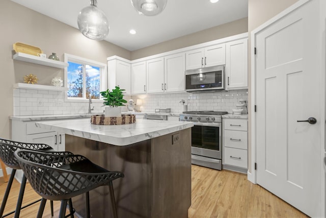 kitchen featuring stainless steel appliances, white cabinets, a kitchen island, light stone countertops, and light wood-type flooring