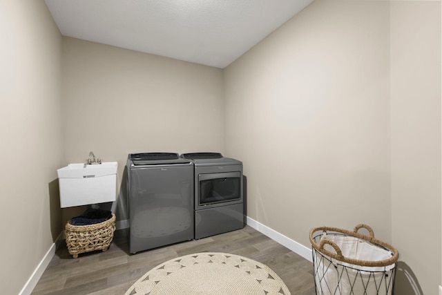 washroom featuring washer and clothes dryer, a sink, wood finished floors, laundry area, and baseboards