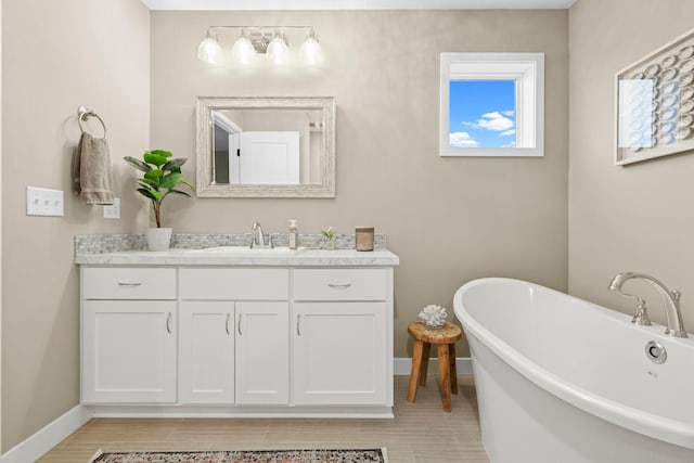 full bath featuring a freestanding bath, vanity, and baseboards