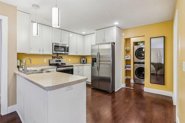 kitchen with appliances with stainless steel finishes, decorative light fixtures, white cabinetry, sink, and stacked washer and clothes dryer