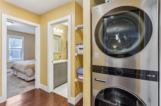 laundry room with stacked washer and dryer, dark hardwood / wood-style floors, and sink