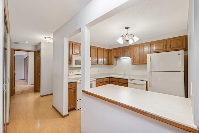 kitchen with sink, decorative light fixtures, light wood-type flooring, a notable chandelier, and white appliances