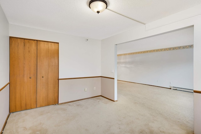 unfurnished bedroom with light carpet, a closet, and a baseboard heating unit