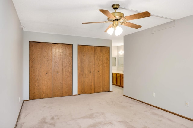 unfurnished bedroom featuring light carpet, multiple closets, connected bathroom, and ceiling fan