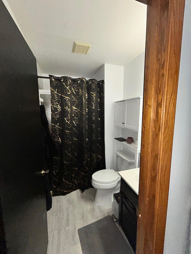 bathroom with hardwood / wood-style flooring, vanity, a shower with curtain, and toilet