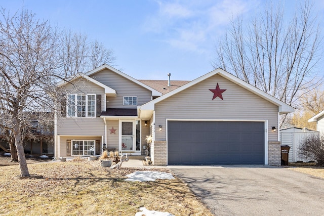 split level home featuring a garage, brick siding, and aphalt driveway