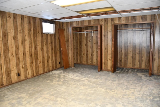 basement with a paneled ceiling and wood walls