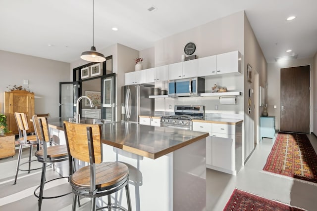 kitchen featuring appliances with stainless steel finishes, pendant lighting, sink, white cabinets, and a kitchen island with sink