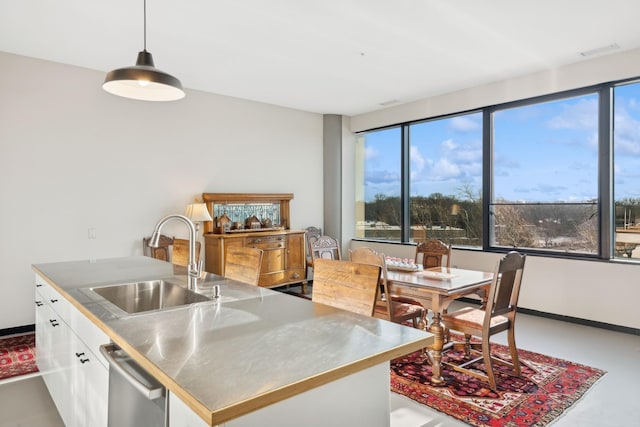 kitchen featuring an island with sink, sink, white cabinets, hanging light fixtures, and stainless steel counters