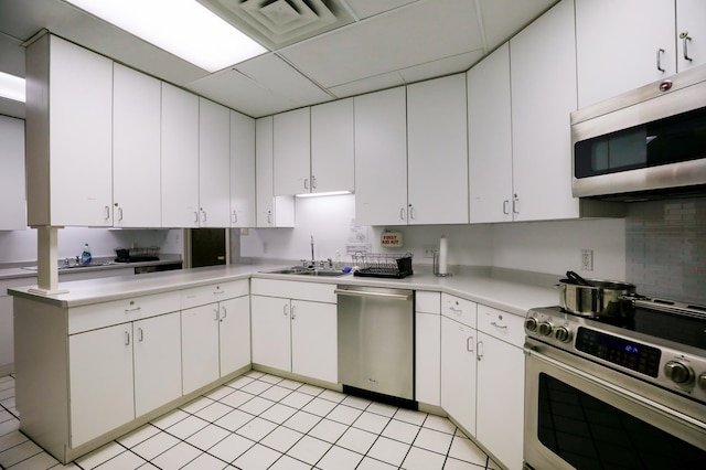 kitchen with appliances with stainless steel finishes, a paneled ceiling, white cabinetry, sink, and backsplash