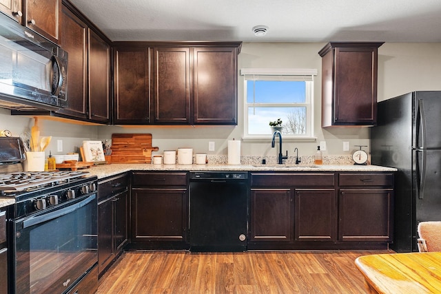 kitchen featuring sink, light stone counters, dark brown cabinets, light hardwood / wood-style floors, and black appliances