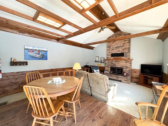 dining area featuring a wainscoted wall, wood walls, a brick fireplace, and vaulted ceiling with beams