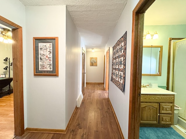 corridor with visible vents, baseboards, a textured ceiling, and wood finished floors