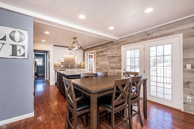 dining room featuring beamed ceiling, dark hardwood / wood-style flooring, sink, and wood walls