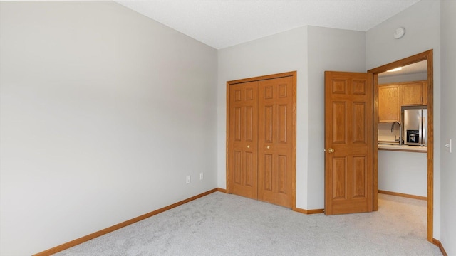 unfurnished bedroom featuring sink, light carpet, stainless steel fridge, and a closet