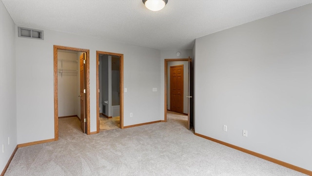 unfurnished bedroom with a spacious closet, light carpet, a closet, and a textured ceiling