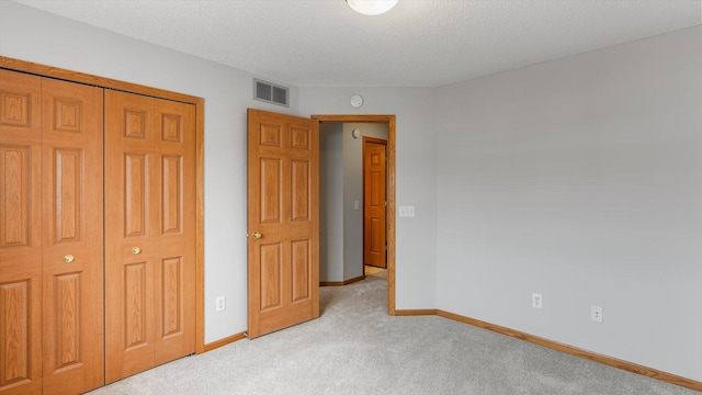 unfurnished bedroom with light carpet, a textured ceiling, and a closet