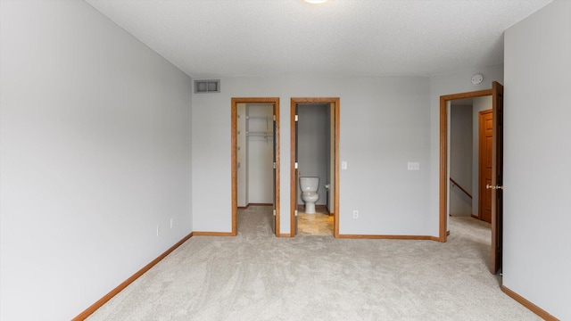 unfurnished bedroom with ensuite bathroom, a walk in closet, light carpet, a textured ceiling, and a closet