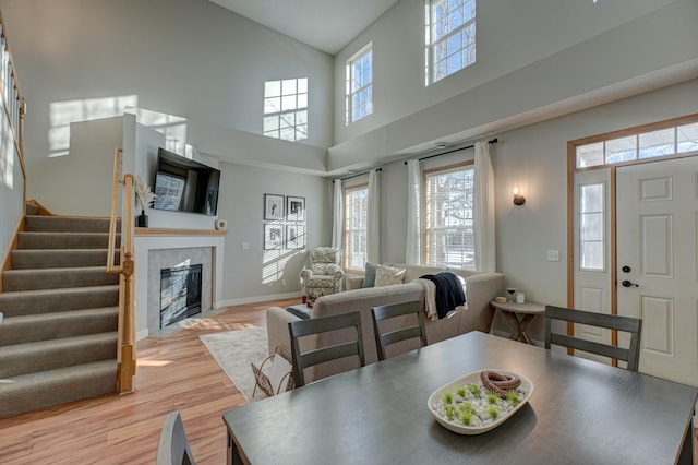 dining space featuring a tiled fireplace, plenty of natural light, a towering ceiling, and light hardwood / wood-style floors