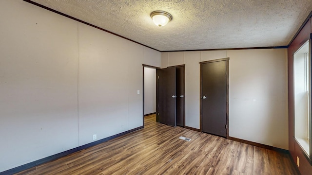 unfurnished bedroom with lofted ceiling, crown molding, wood-type flooring, and a textured ceiling