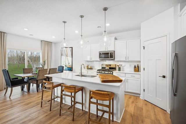 kitchen with pendant lighting, sink, white cabinets, stainless steel appliances, and a center island with sink