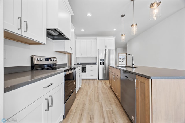 kitchen featuring decorative light fixtures, stainless steel appliances, white cabinets, and a center island with sink