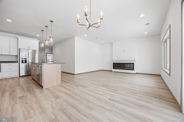 kitchen featuring appliances with stainless steel finishes, pendant lighting, white cabinets, a kitchen island with sink, and light hardwood / wood-style flooring