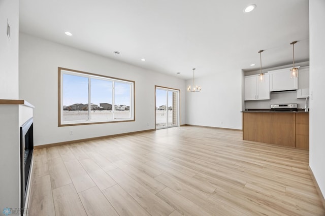 unfurnished living room with an inviting chandelier and light hardwood / wood-style flooring