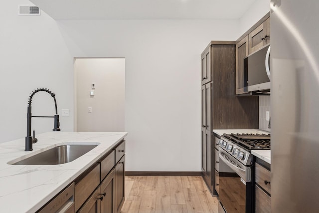 kitchen with sink, light hardwood / wood-style flooring, appliances with stainless steel finishes, backsplash, and light stone counters