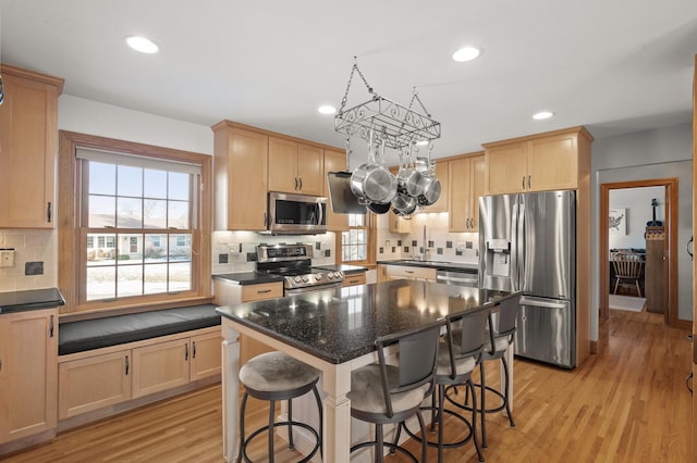 kitchen featuring a center island, light wood-type flooring, light brown cabinets, stainless steel appliances, and decorative backsplash