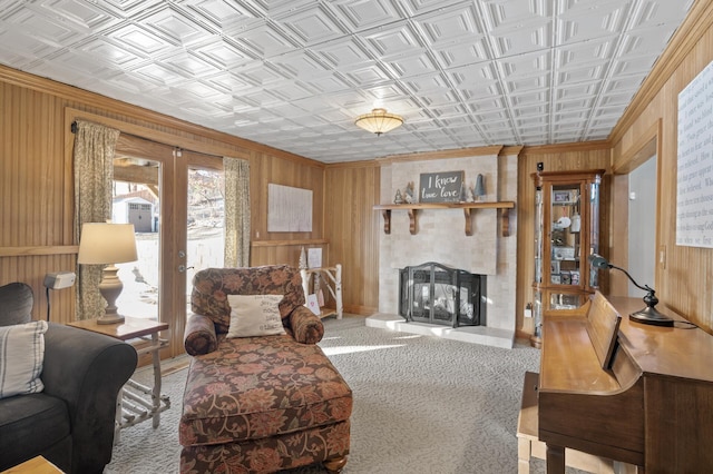 living room featuring crown molding, wooden walls, carpet flooring, a large fireplace, and french doors