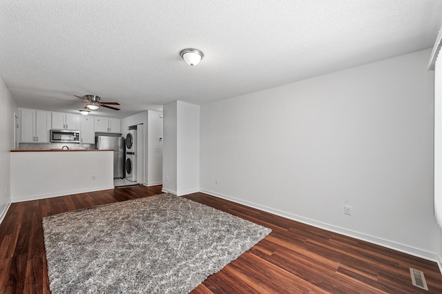 unfurnished living room with dark wood-type flooring, ceiling fan, stacked washer / dryer, and a textured ceiling