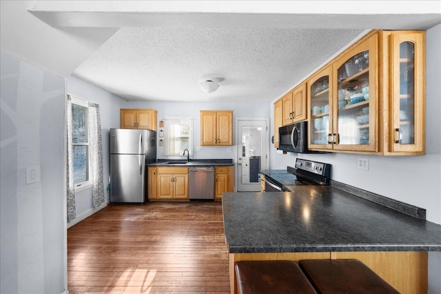 kitchen with sink, dark wood-type flooring, stainless steel appliances, a textured ceiling, and kitchen peninsula