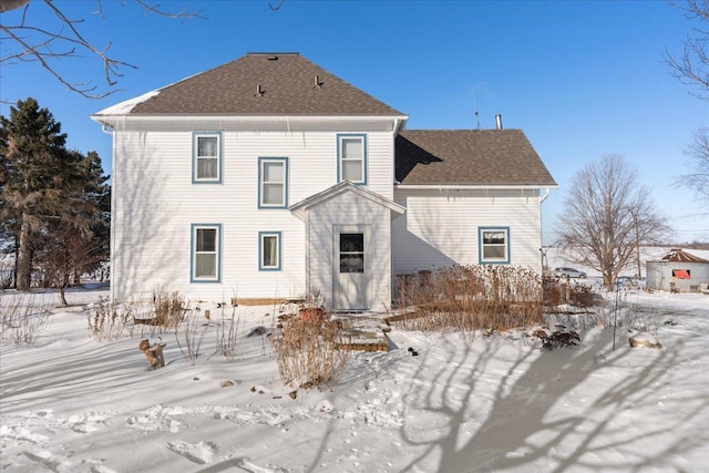 snow covered back of property featuring a shingled roof