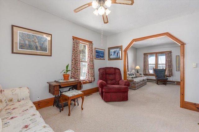 living area with a baseboard heating unit, light colored carpet, baseboards, and a ceiling fan