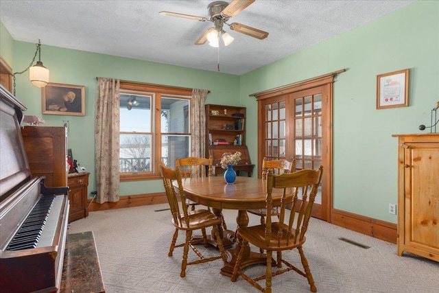 dining space with a textured ceiling, ceiling fan, light carpet, and visible vents