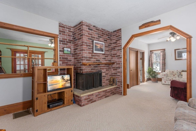 carpeted living room with visible vents, a ceiling fan, a brick fireplace, a textured ceiling, and baseboards