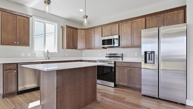 kitchen with sink, a center island, hanging light fixtures, light hardwood / wood-style flooring, and appliances with stainless steel finishes