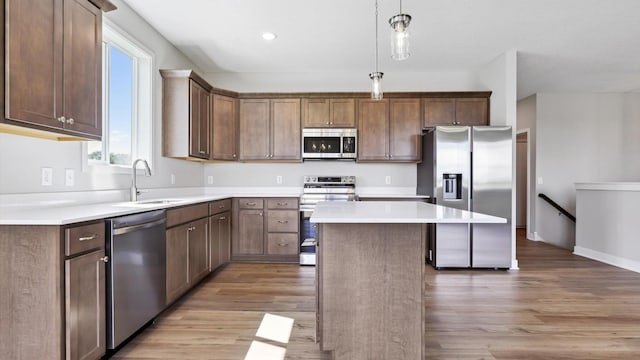 kitchen featuring pendant lighting, sink, stainless steel appliances, a center island, and light wood-type flooring