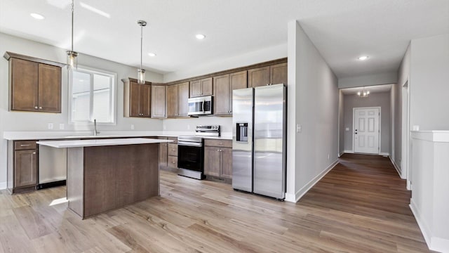 kitchen featuring stainless steel appliances, decorative light fixtures, light hardwood / wood-style floors, and a kitchen island