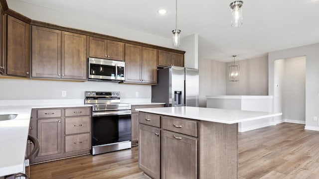 kitchen featuring dark brown cabinets, light wood-type flooring, appliances with stainless steel finishes, a kitchen island, and pendant lighting