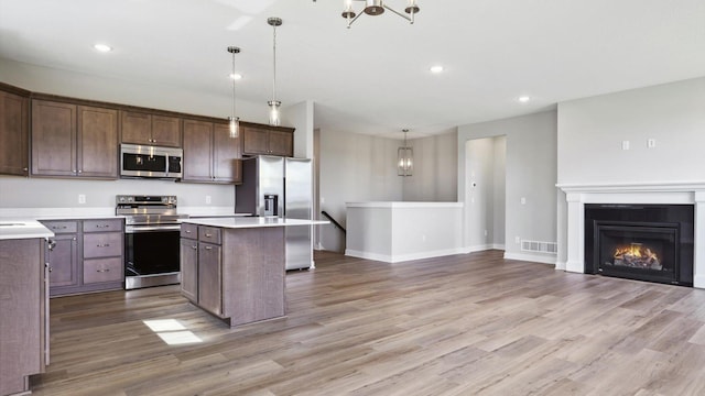 kitchen with hanging light fixtures, a center island, light hardwood / wood-style floors, stainless steel appliances, and dark brown cabinets