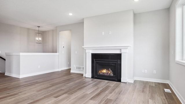 unfurnished living room featuring an inviting chandelier and light wood-type flooring