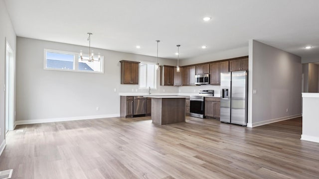 kitchen with stainless steel appliances, decorative light fixtures, wood-type flooring, and a kitchen island