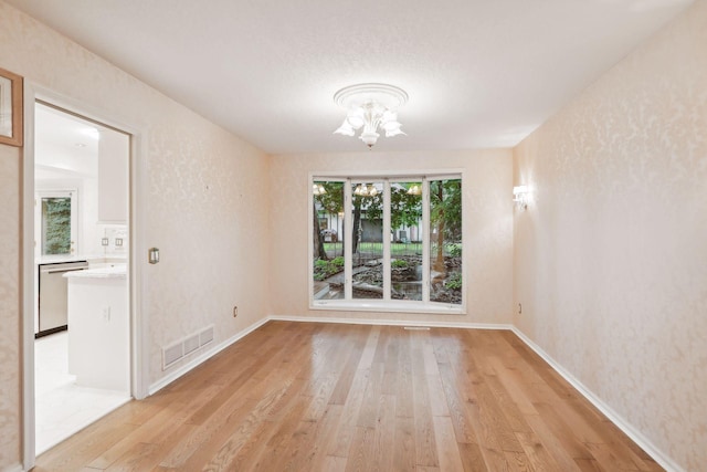 spare room with a chandelier, a textured ceiling, and light wood-type flooring