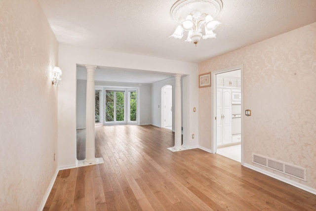 empty room featuring ornate columns, wood-type flooring, a textured ceiling, and a chandelier