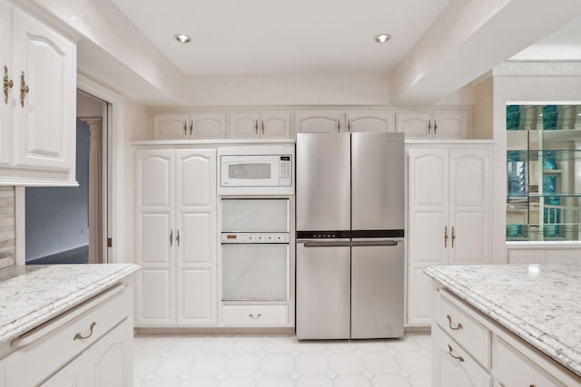 kitchen featuring light stone counters, stainless steel fridge, wall oven, white microwave, and white cabinets