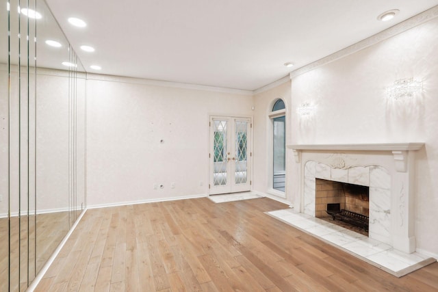 unfurnished living room with crown molding, wood-type flooring, a premium fireplace, and french doors