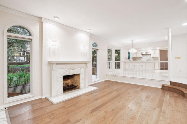 unfurnished living room with crown molding, a notable chandelier, a fireplace, and light hardwood / wood-style floors