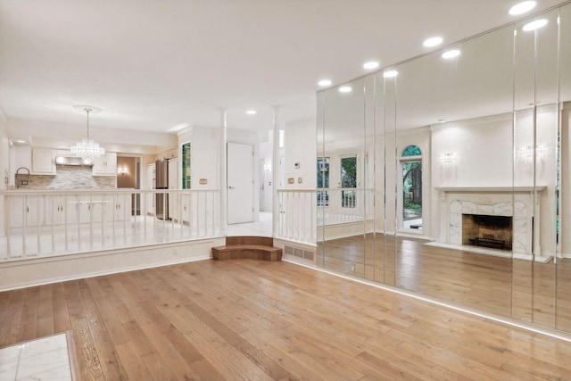 unfurnished living room with an inviting chandelier, a fireplace, sink, and light wood-type flooring